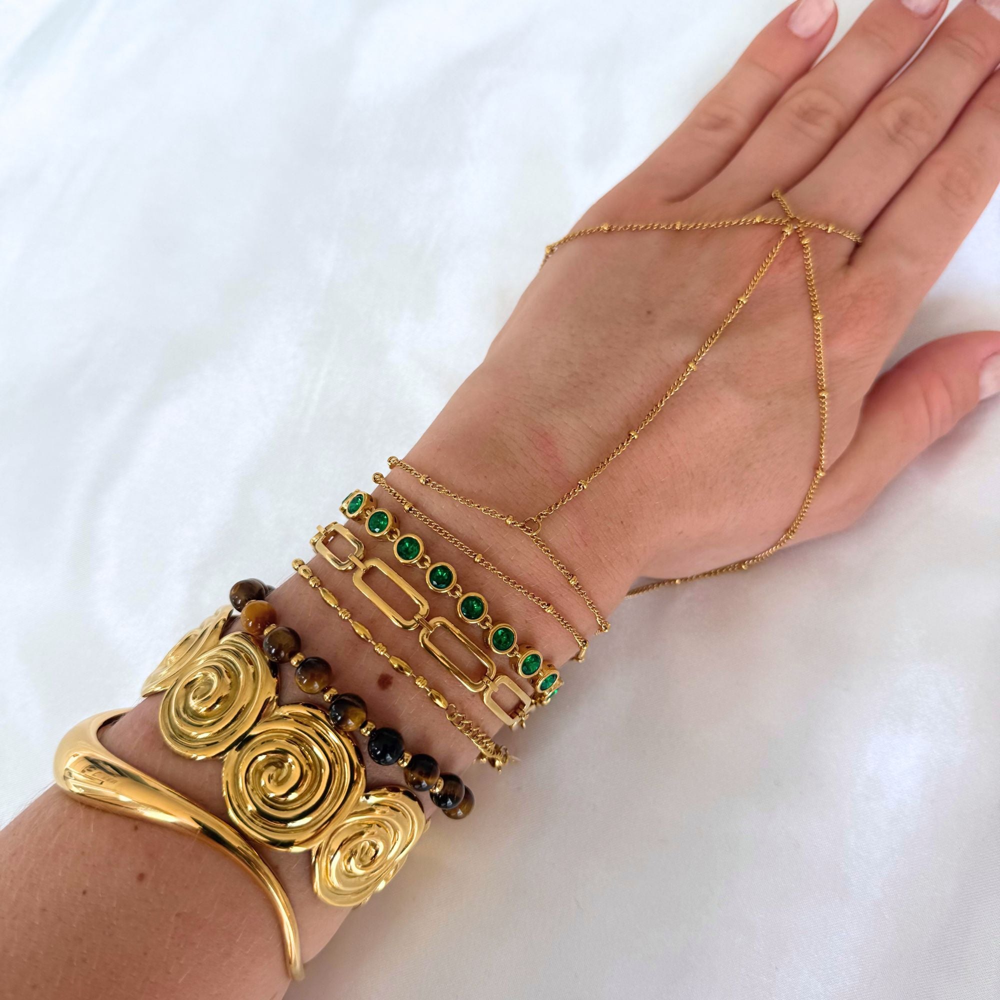Hand wearing multiple gold bracelets with green gemstones on a white background