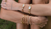 Person wearing multiple gold bracelets on a grassy background