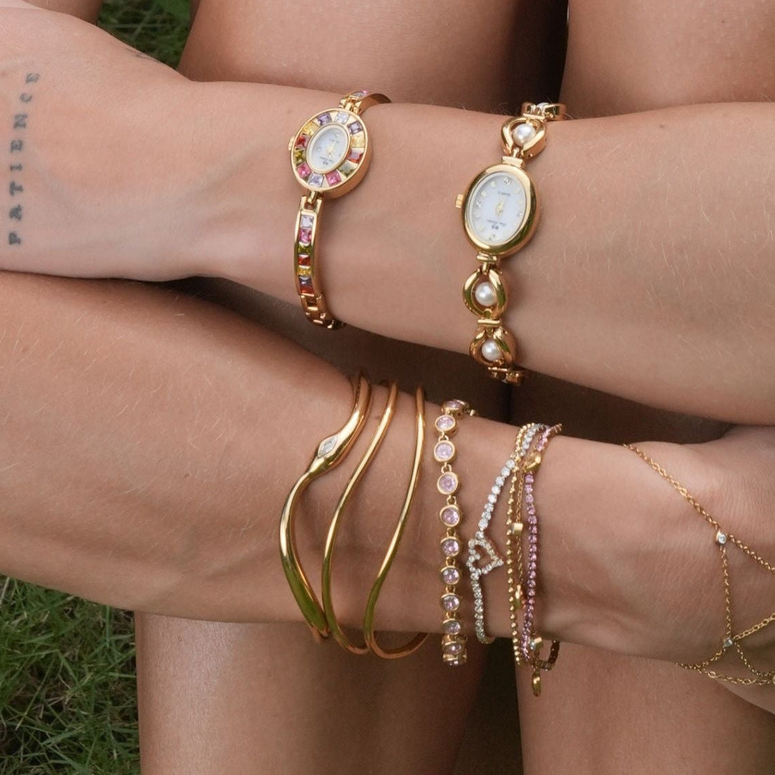 Person wearing multiple gold bracelets on a grassy background