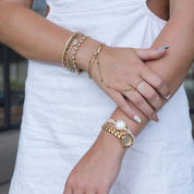Close-up of a person's hands wearing multiple gold bracelets on a blurred outdoor background