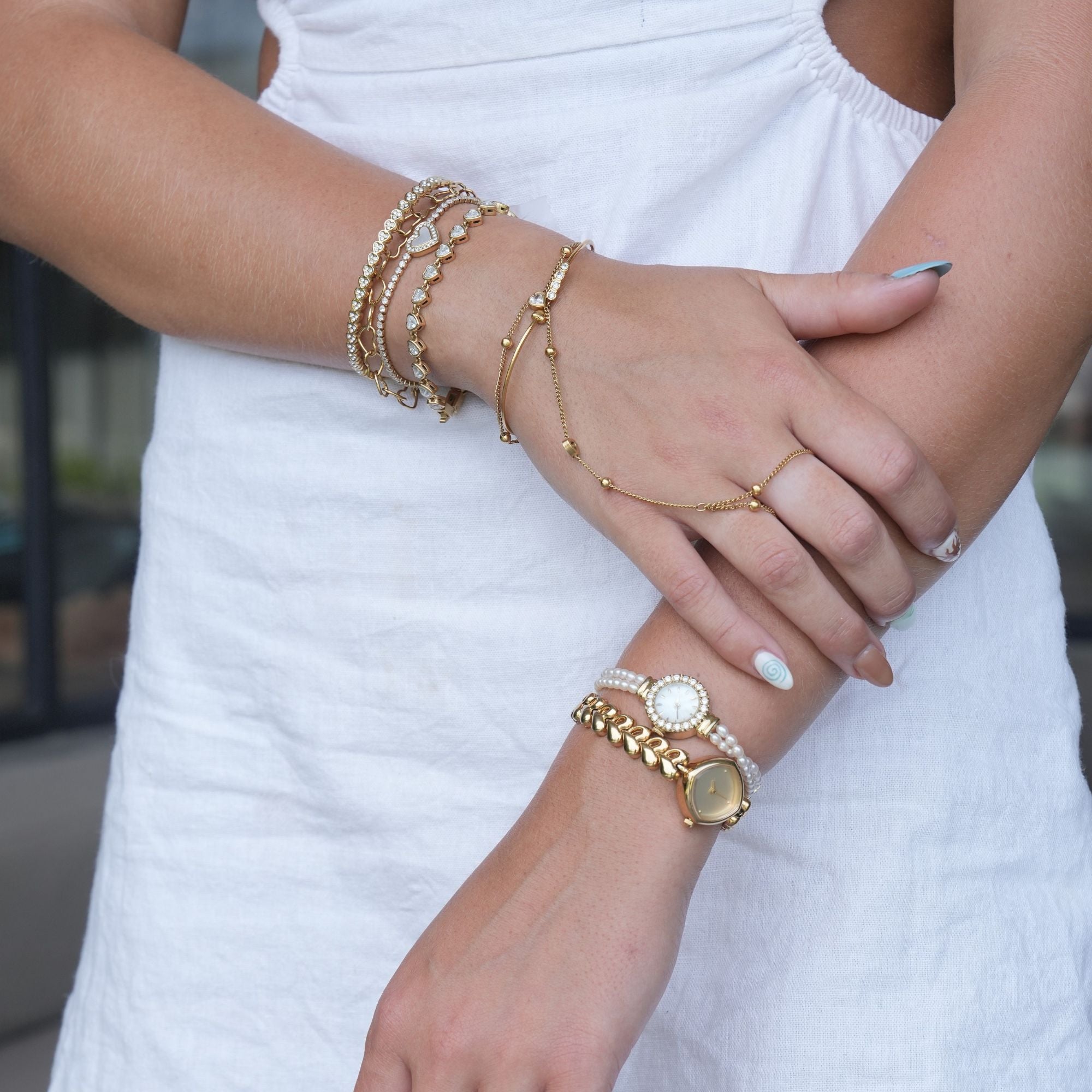 Close-up of a person's hands wearing multiple gold bracelets on a blurred outdoor background