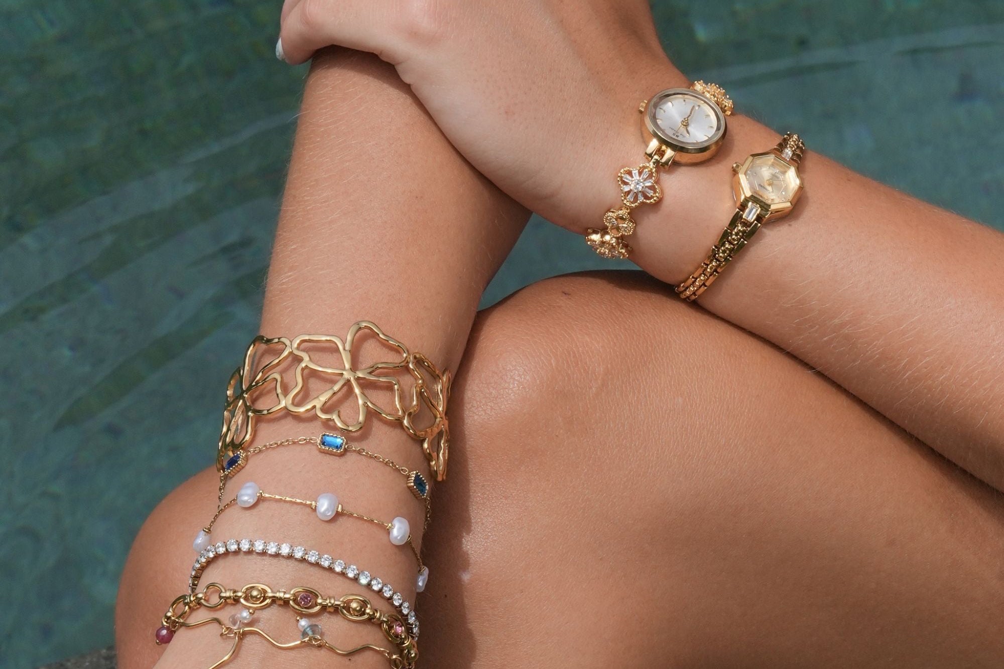 Close-up of a person's arm with multiple gold bracelets and rings against a blurred natural background